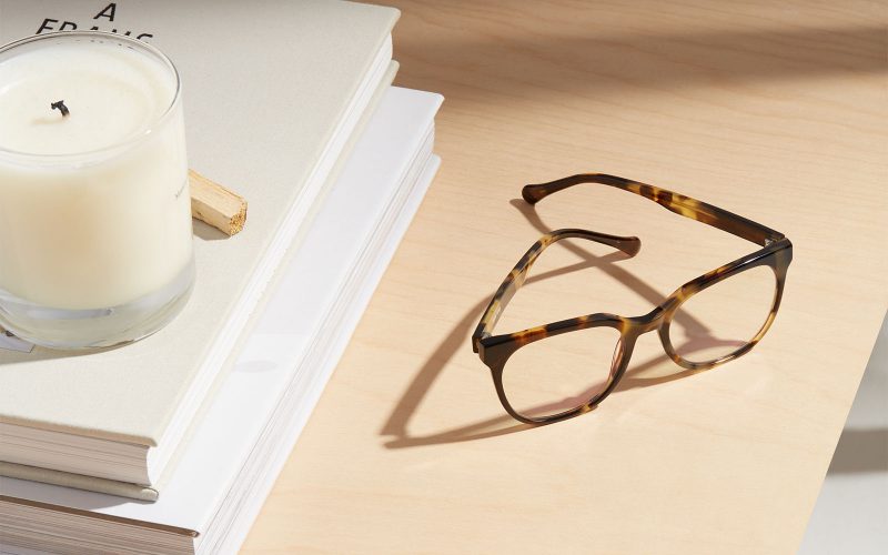 Image of brown eyeglasses next to a candle and book