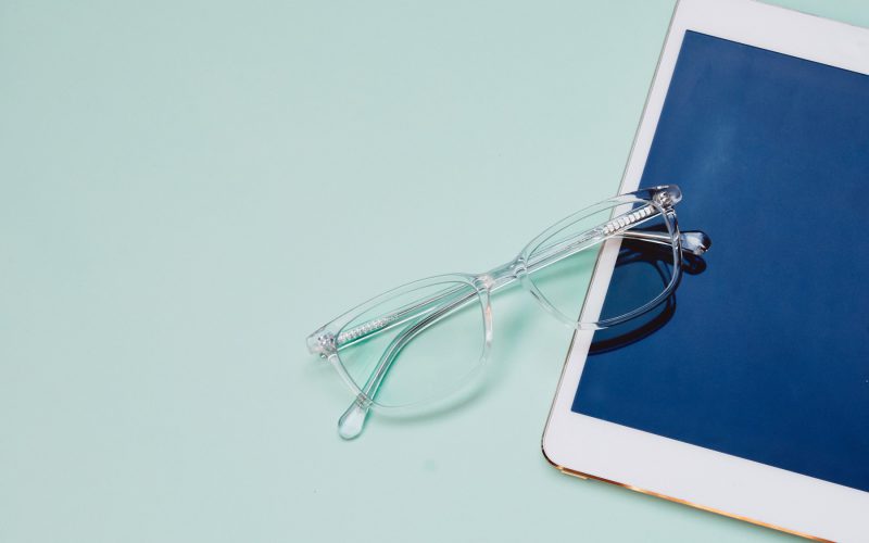 A pair of clear eyeglasses on a white iPad over a mint green background