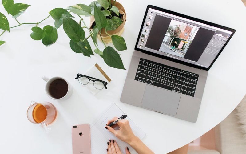 A desk setup with a computer, tea, phone, glasses and plant