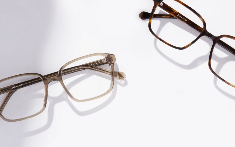 A pair of square soft champagne colored eyeglasses next to a pair of brown square eyeglasses