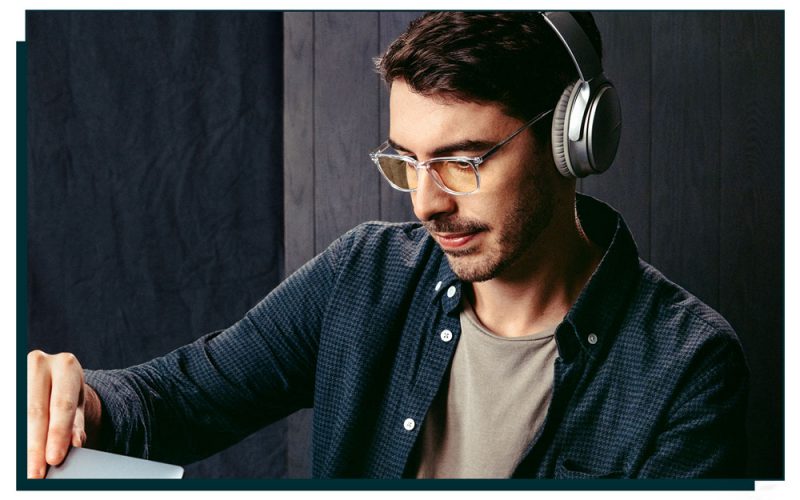 image of man wearing glasses and headphones looking towards a laptop